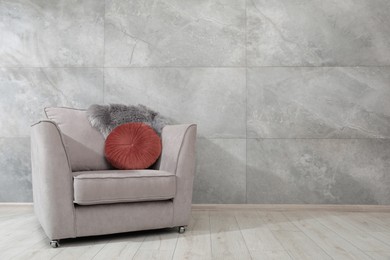 Photo of Comfortable armchair, fluffy blanket and cushion near gray marble wall. Space for text
