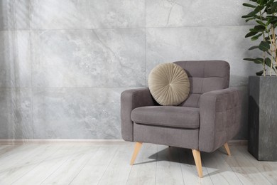 Photo of Comfortable armchair with cushion and houseplant near gray marble wall. Space for text