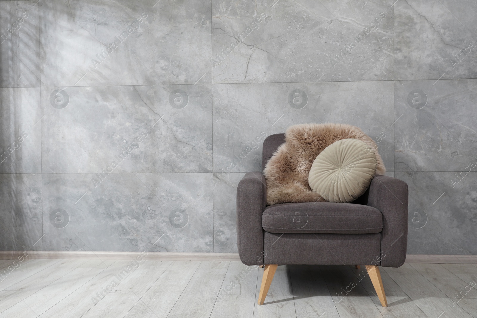 Photo of Comfortable armchair, fluffy blanket and cushion near gray marble wall. Space for text