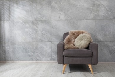 Photo of Comfortable armchair, fluffy blanket and cushion near gray marble wall. Space for text