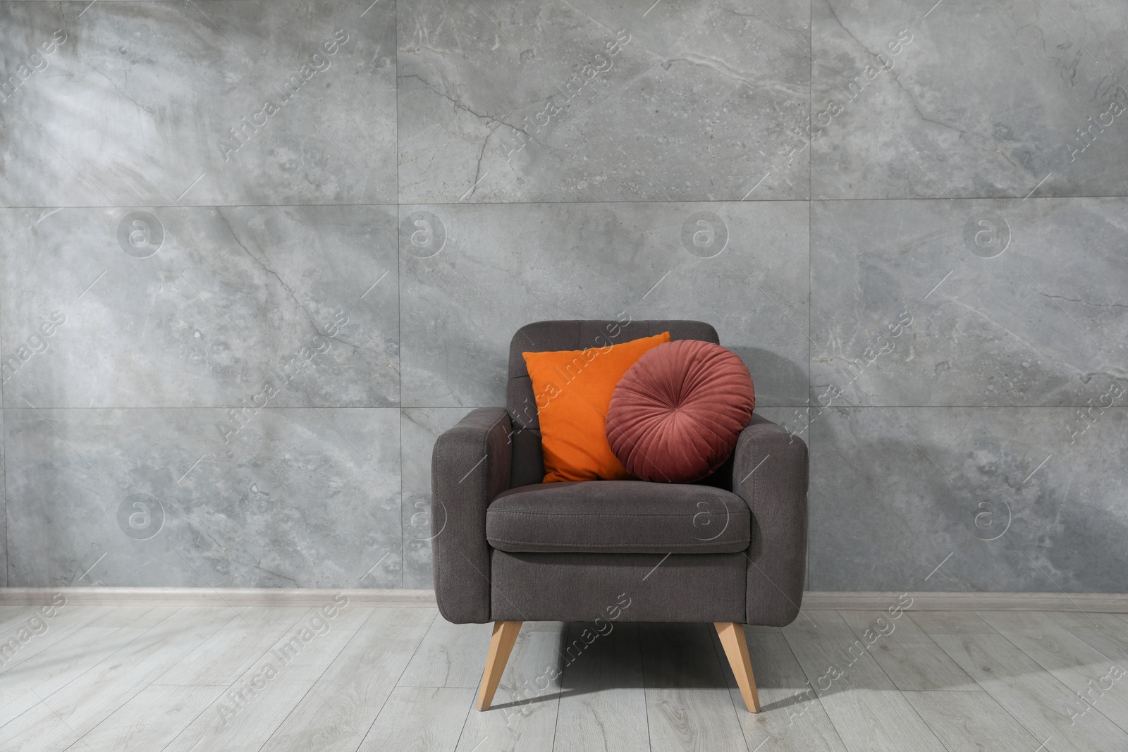 Photo of Comfortable armchair and cushions near gray marble wall