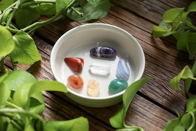Photo of Aura. Different natural mineral stones in bowl and green leaves on wooden table, closeup