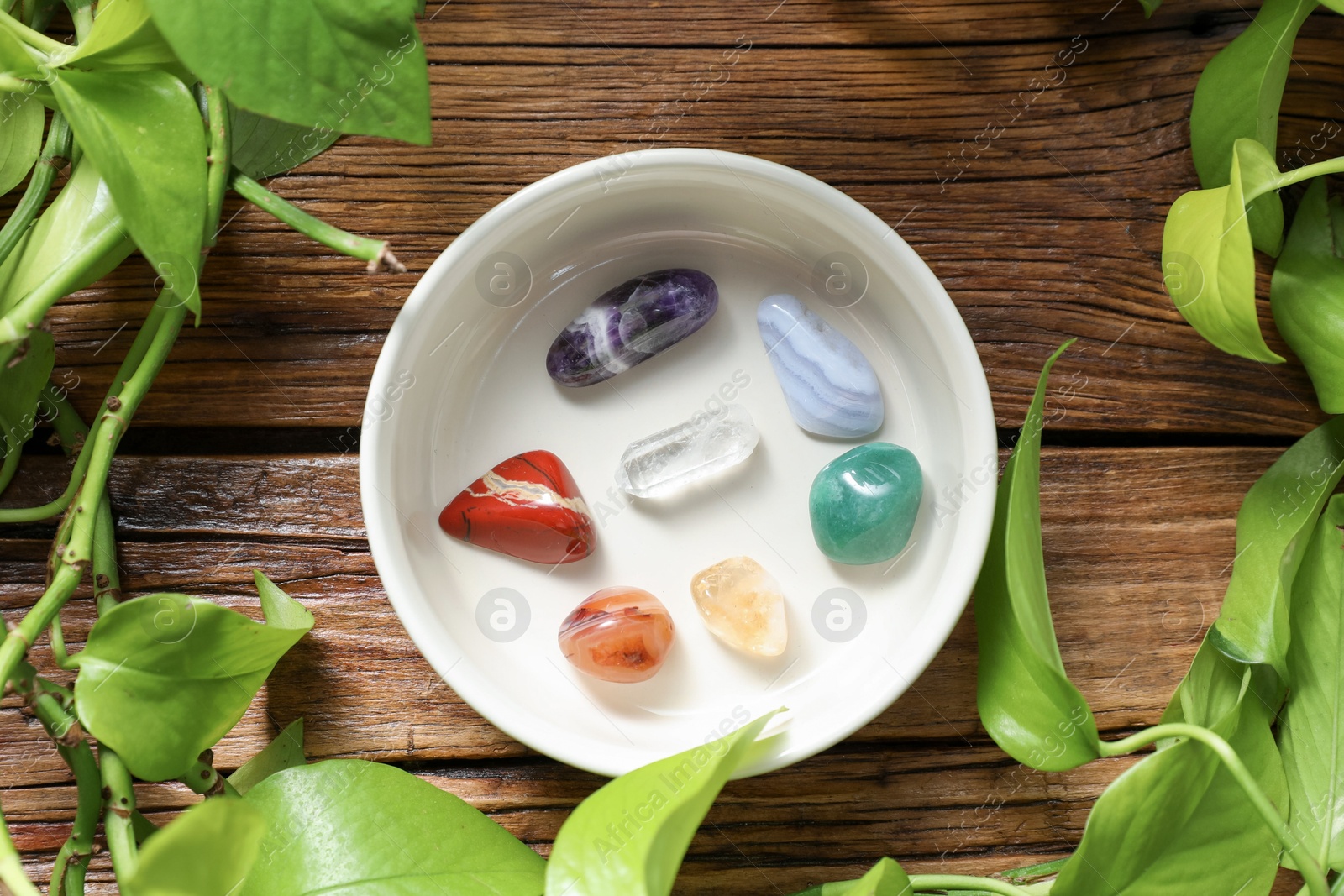 Photo of Aura. Different natural mineral stones in bowl and green leaves on wooden table, flat lay