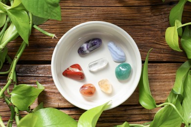 Photo of Aura. Different natural mineral stones in bowl and green leaves on wooden table, flat lay