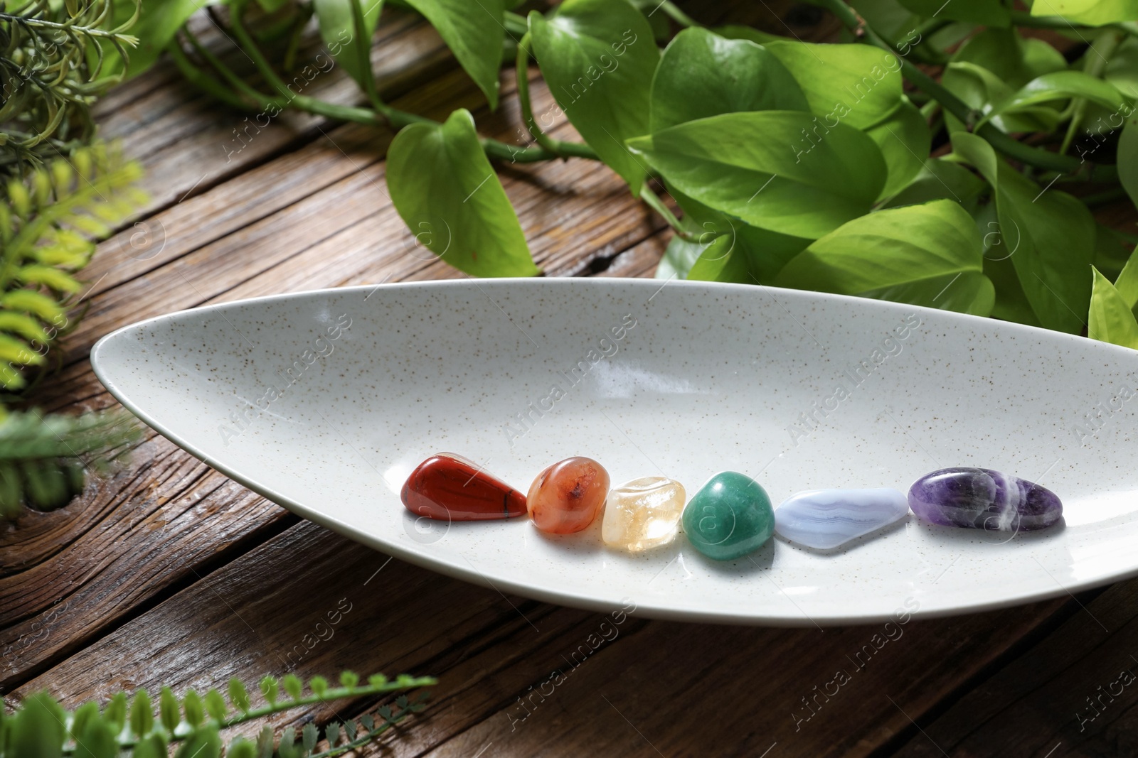Photo of Aura. Different natural mineral stones and green leaves on wooden table, closeup