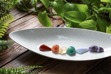 Photo of Aura. Different natural mineral stones and green leaves on wooden table, closeup