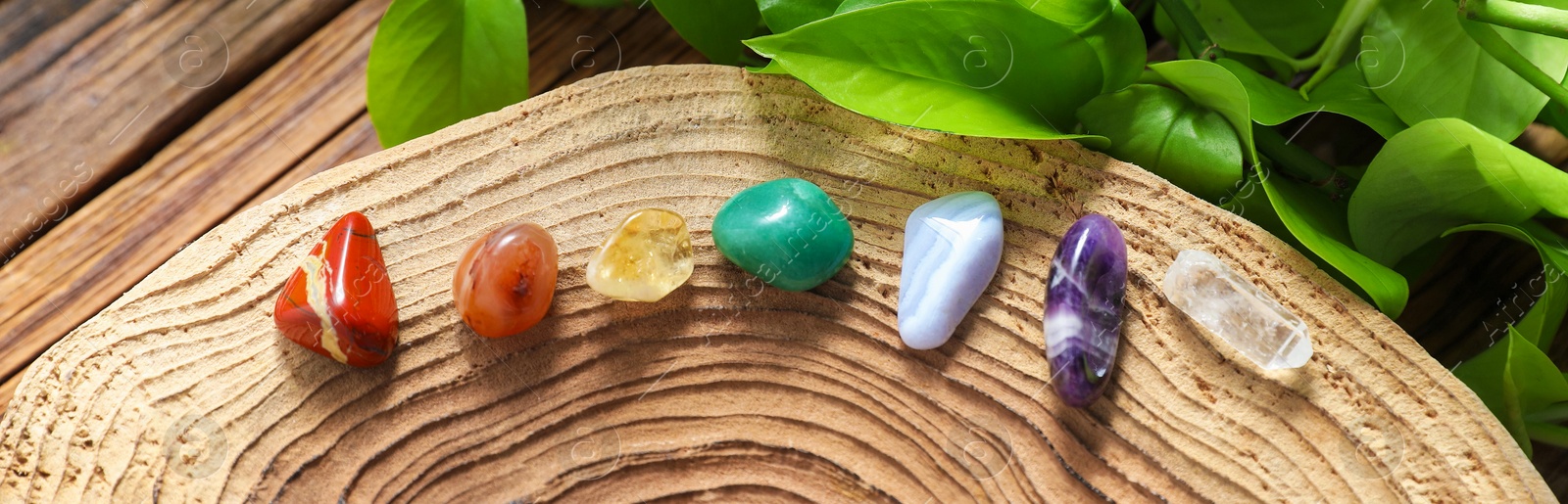 Photo of Aura. Different natural mineral stones and green leaves on wooden table, flat lay