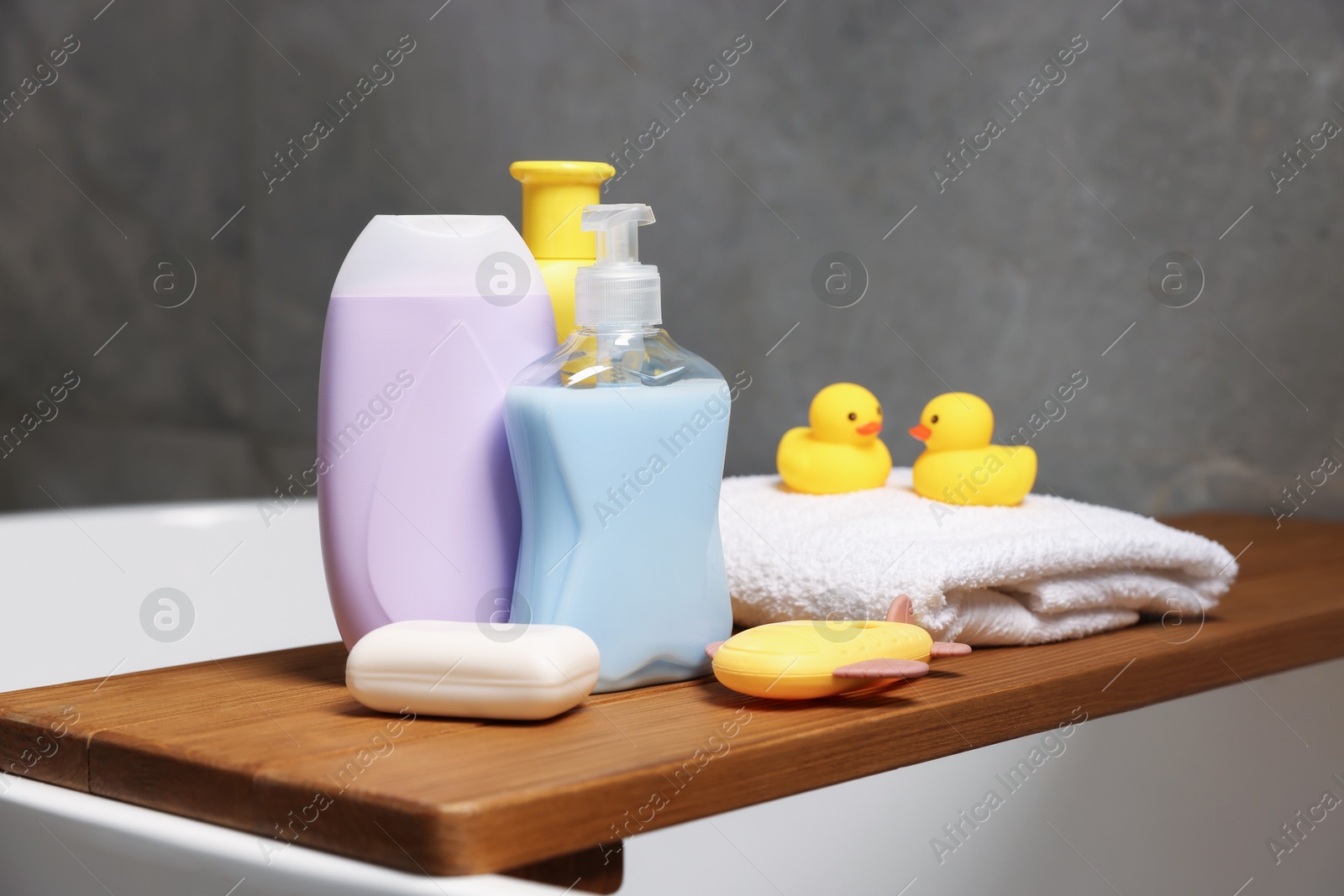 Photo of Baby accessories and bathing products on wooden tray in bathtub indoors, closeup
