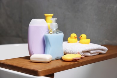 Photo of Baby accessories and bathing products on wooden tray in bathtub indoors, closeup