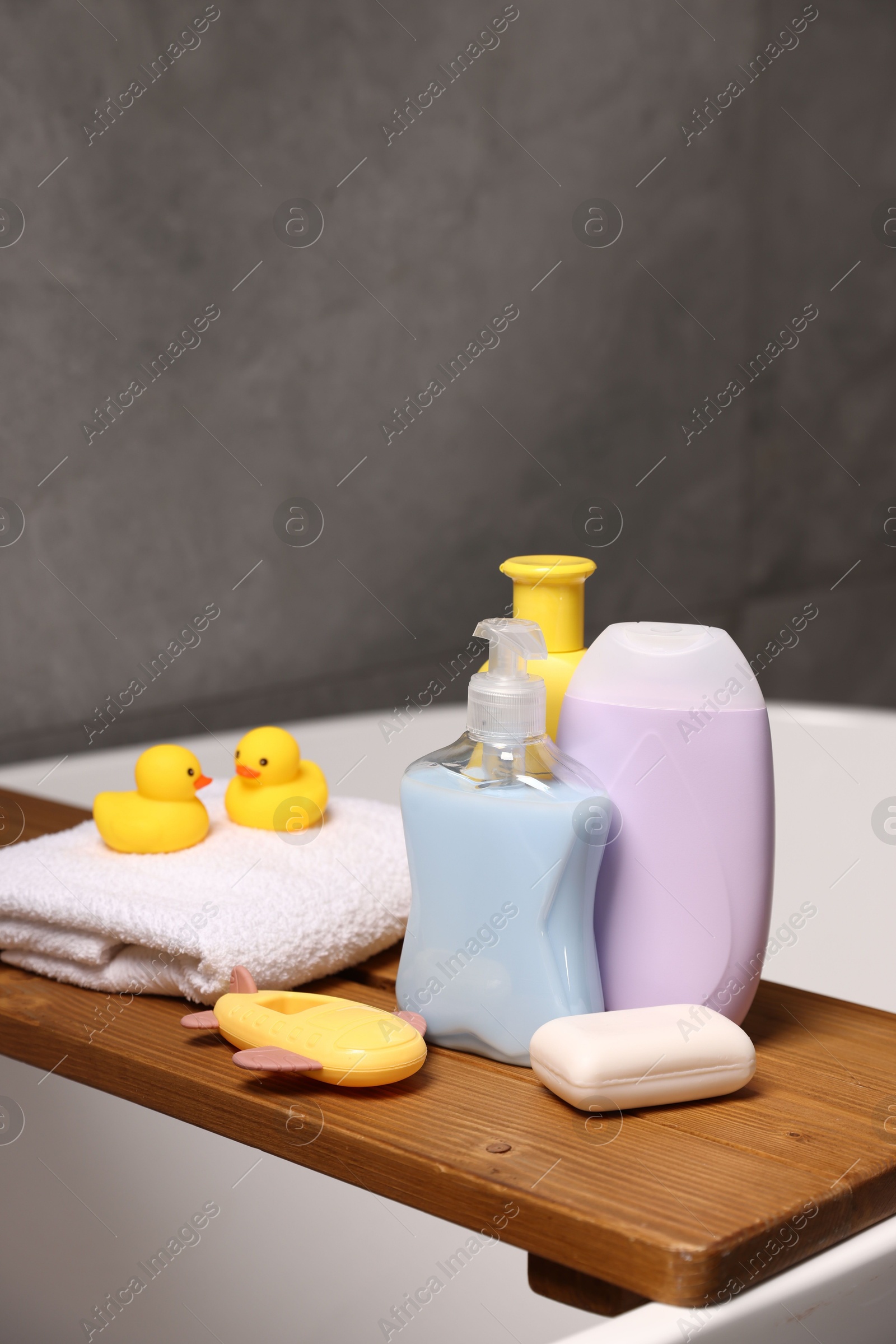 Photo of Baby accessories and bathing products on wooden tray in bathtub indoors, closeup