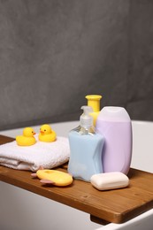 Photo of Baby accessories and bathing products on wooden tray in bathtub indoors, closeup