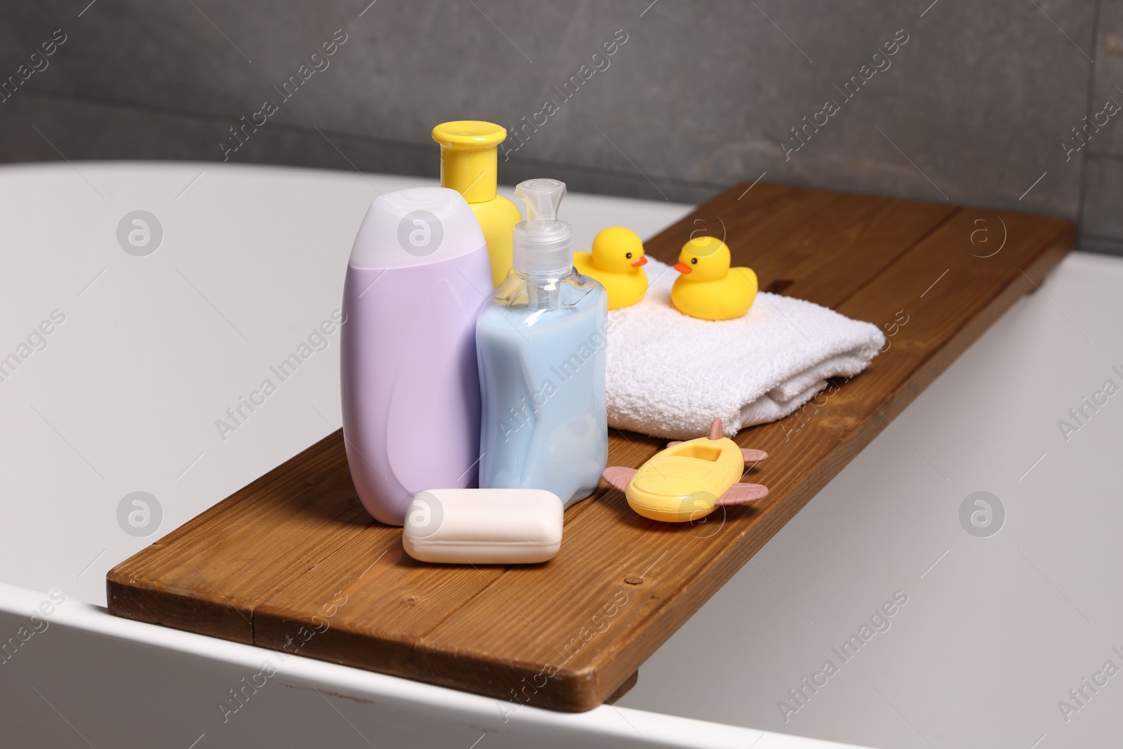 Photo of Baby accessories and bathing products on wooden tray in bathtub indoors, closeup