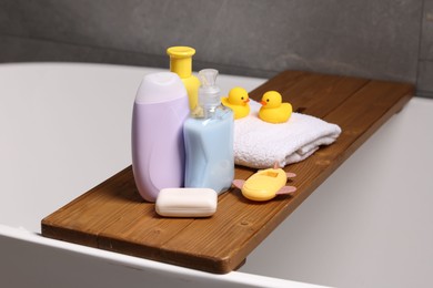 Photo of Baby accessories and bathing products on wooden tray in bathtub indoors, closeup