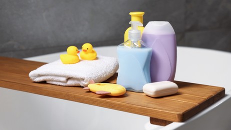 Photo of Baby accessories and bathing products on wooden tray in bathtub indoors, closeup