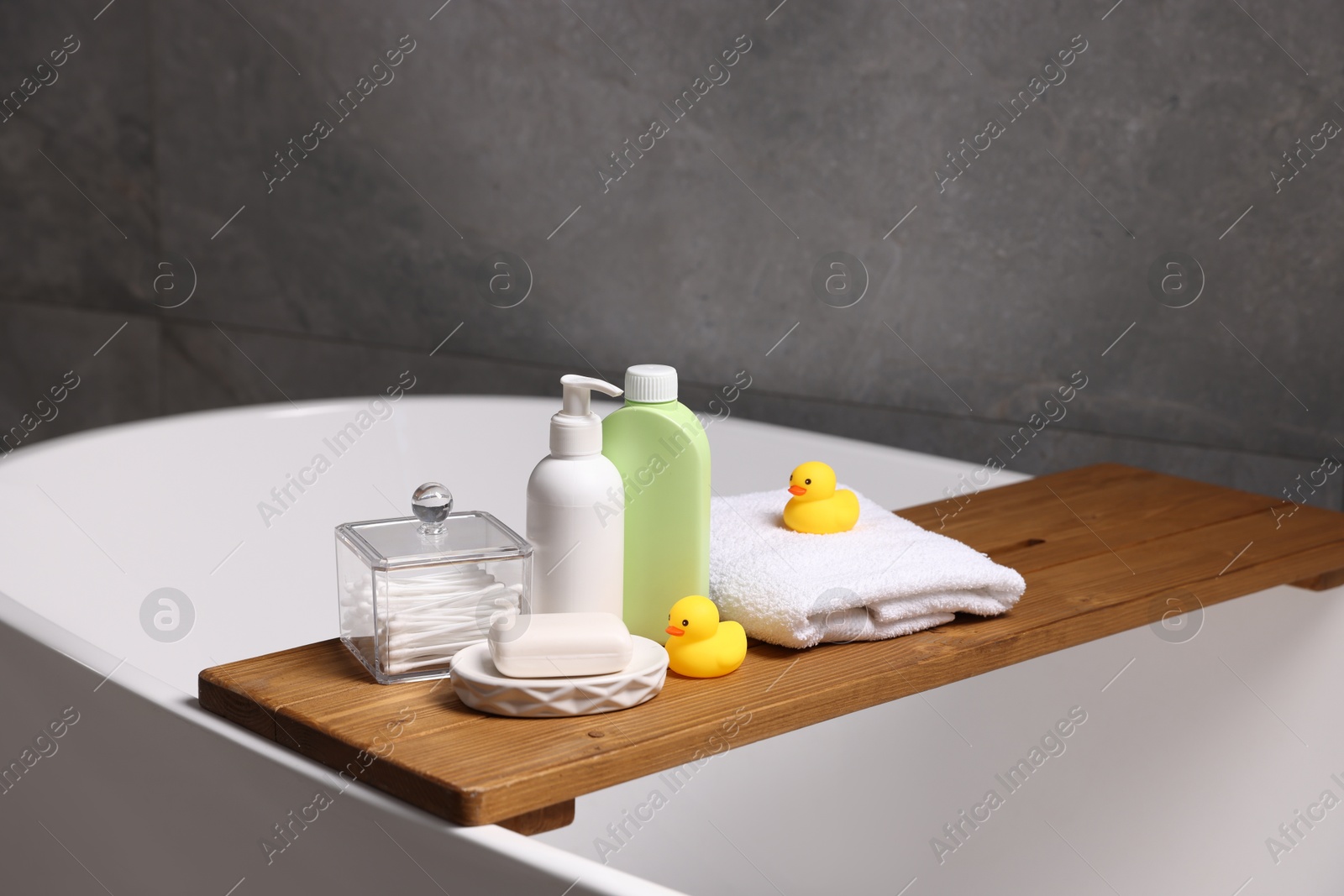 Photo of Baby accessories and bathing products on wooden tray in bathtub indoors, closeup