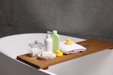 Photo of Baby accessories and bathing products on wooden tray in bathtub indoors, closeup