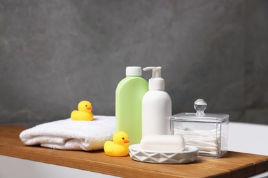 Photo of Baby accessories and bathing products on wooden tray in bathtub indoors, closeup