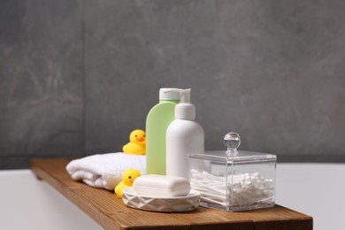 Photo of Baby accessories and bathing products on wooden tray in bathtub indoors, closeup