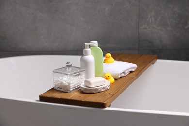 Photo of Baby accessories and bathing products on wooden tray in bathtub indoors, closeup