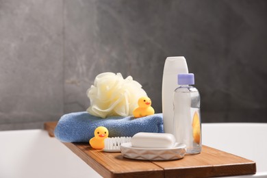 Photo of Baby accessories and bathing products on wooden tray in bathtub indoors, closeup