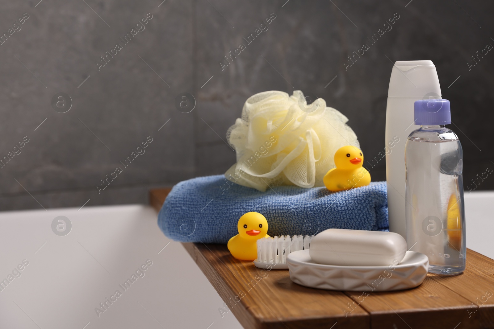 Photo of Baby accessories and bathing products on wooden tray in bathtub indoors, closeup