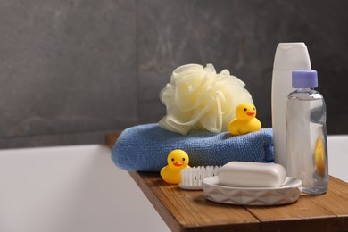 Photo of Baby accessories and bathing products on wooden tray in bathtub indoors, closeup