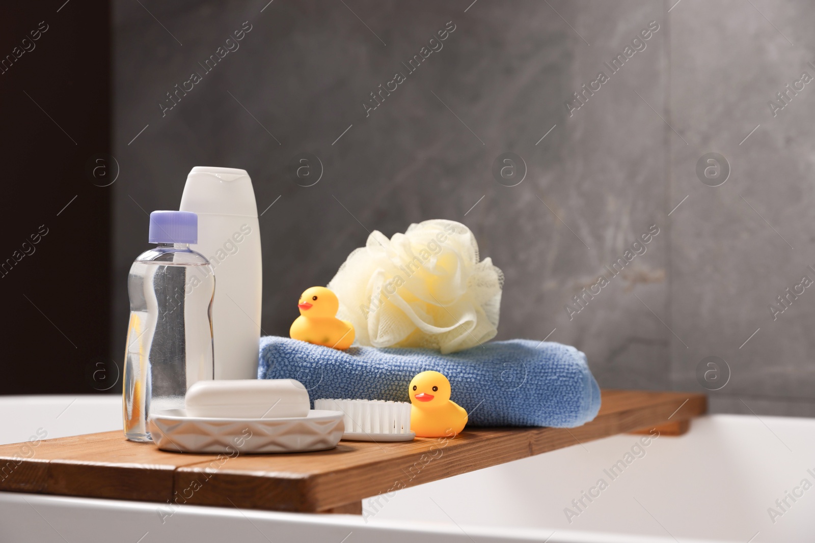 Photo of Baby accessories and bathing products on wooden tray in bathtub indoors, closeup
