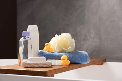 Photo of Baby accessories and bathing products on wooden tray in bathtub indoors, closeup