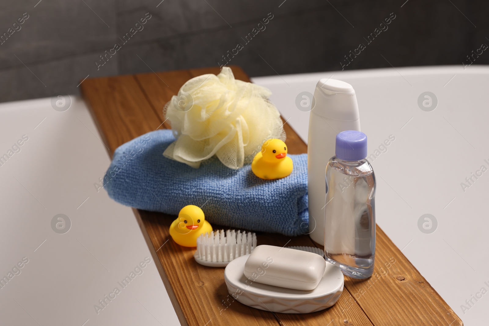 Photo of Baby accessories and bathing products on wooden tray in bathtub indoors, closeup