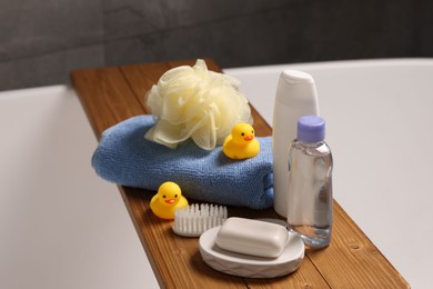 Photo of Baby accessories and bathing products on wooden tray in bathtub indoors, closeup