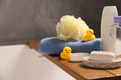 Photo of Baby accessories and bathing products on wooden tray in bathtub indoors, closeup