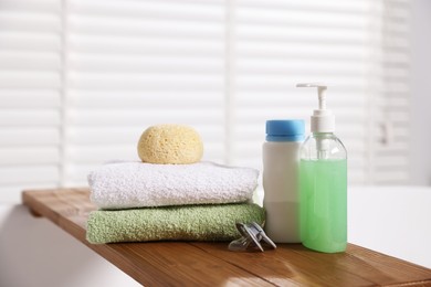 Photo of Baby accessories and bathing products on wooden tray in bathtub indoors, closeup