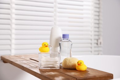 Photo of Baby accessories and bathing products on wooden tray in bathtub indoors