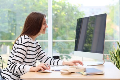 Photo of Woman using computer at wooden desk indoors. Home workplace