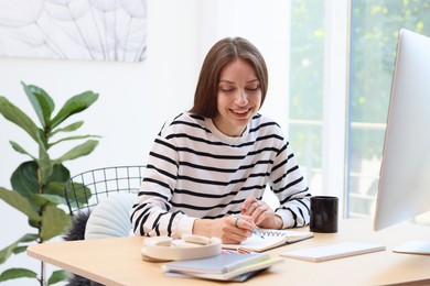 Photo of Woman writing and using computer at wooden desk indoors. Home workplace