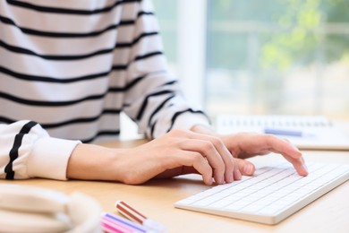 Photo of Woman using computer at wooden desk indoors, closeup. Home workplace