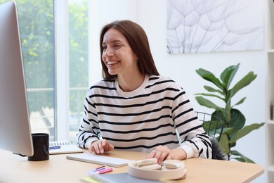 Photo of Woman using computer at wooden desk indoors. Home workplace