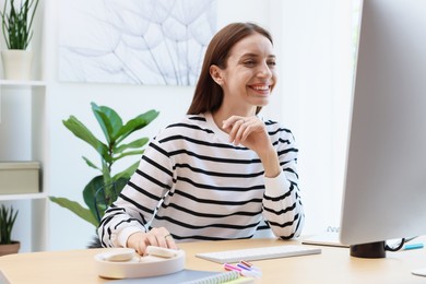 Photo of Woman using computer at wooden desk indoors. Home workplace