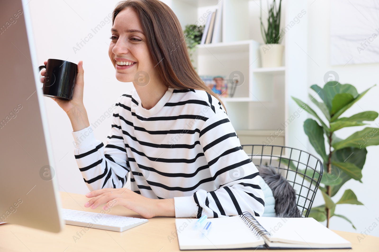 Photo of Woman with coffee using computer at wooden desk indoors. Home workplace