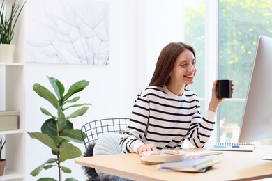 Photo of Woman with coffee using computer at wooden desk indoors. Home workplace