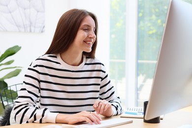 Photo of Woman using computer at wooden desk indoors. Home workplace