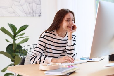 Photo of Woman using computer at wooden desk indoors. Home workplace