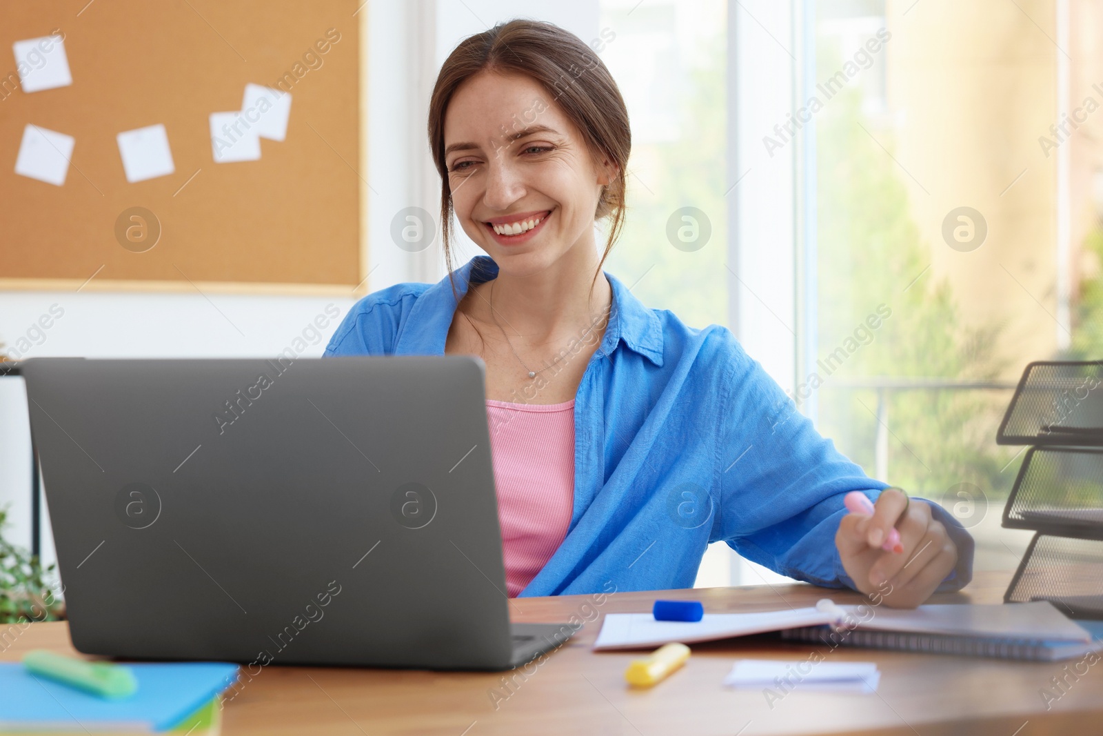 Photo of Woman using laptop at wooden desk indoors. Home workplace
