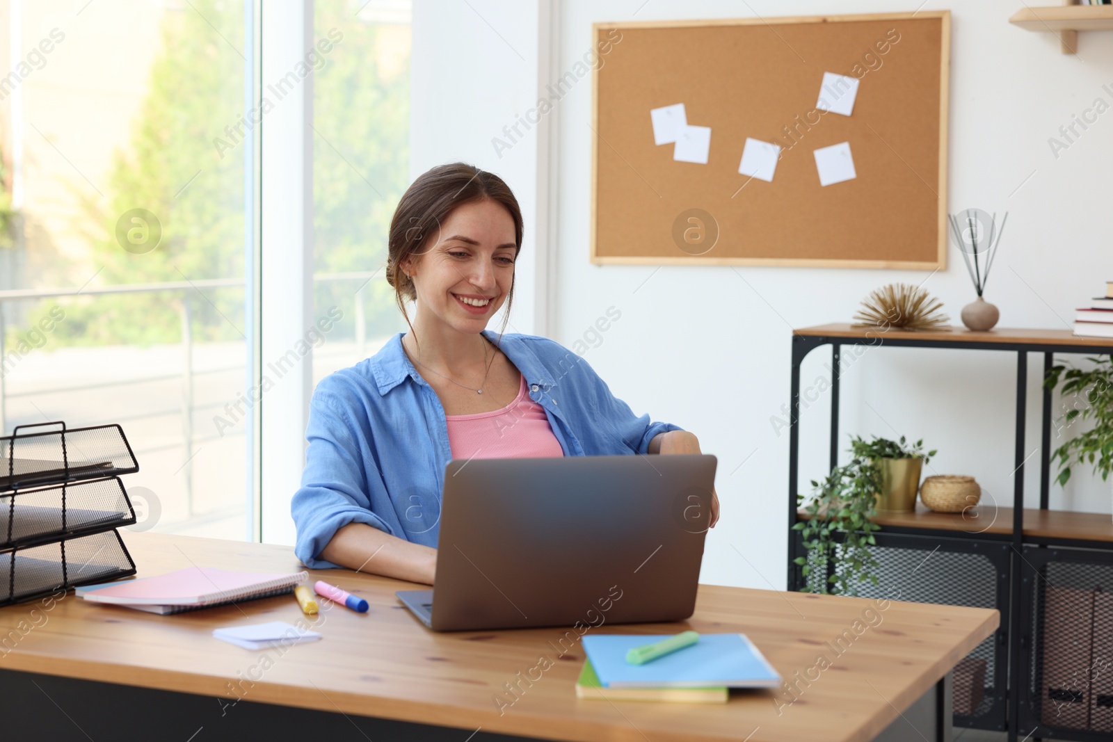 Photo of Woman using laptop at wooden desk indoors. Home workplace