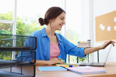Photo of Woman using laptop at wooden desk indoors. Home workplace