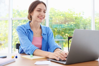 Photo of Woman using laptop at wooden desk indoors. Home workplace