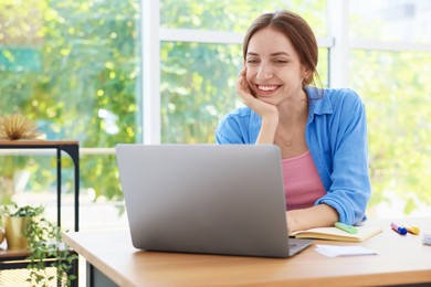 Photo of Woman using laptop at wooden desk indoors. Home workplace