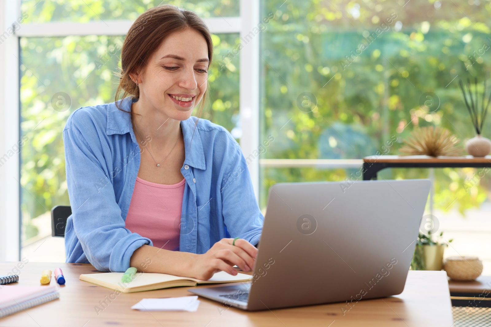 Photo of Woman using laptop at wooden desk indoors. Home workplace