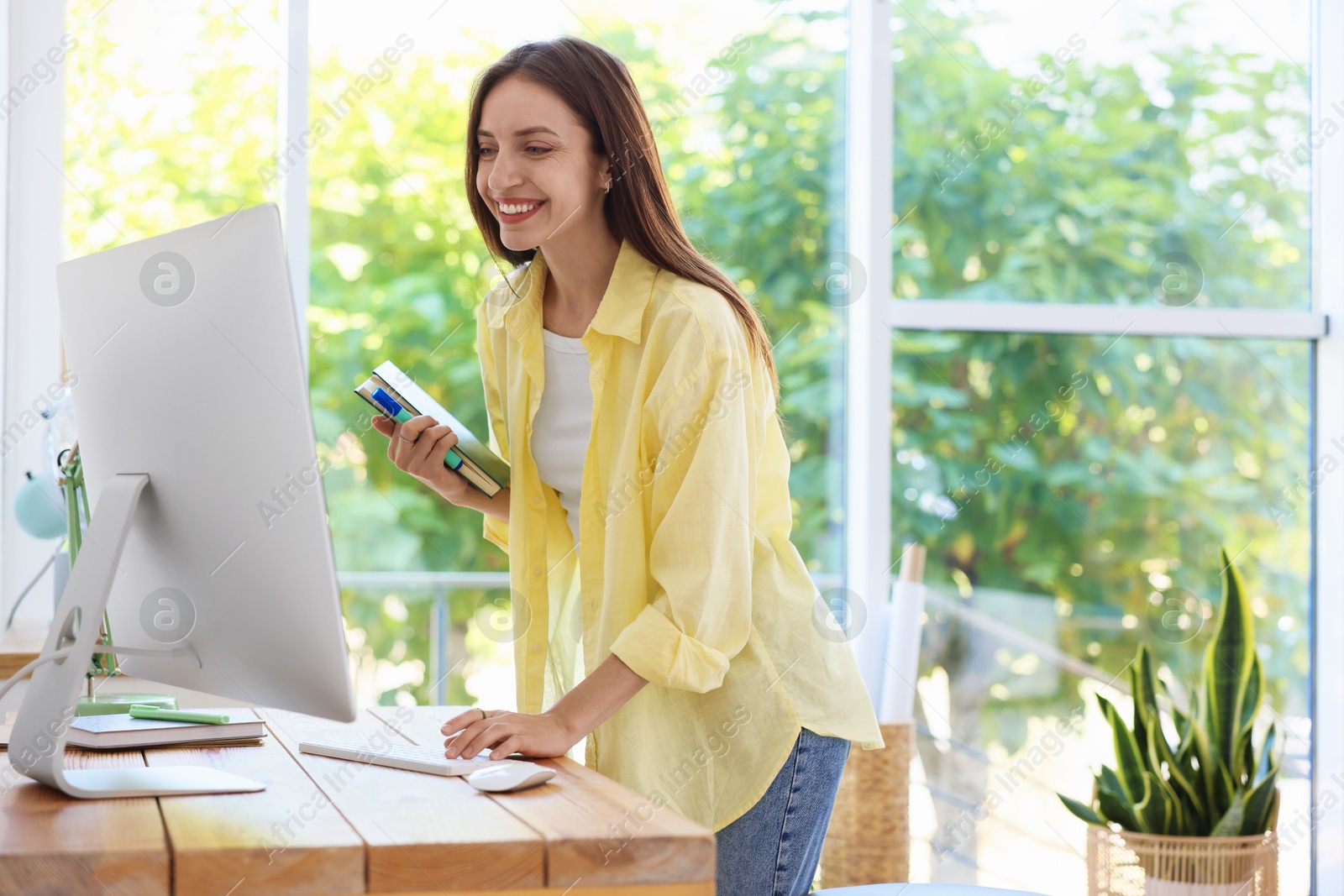 Photo of Woman using computer at wooden desk indoors. Home workplace