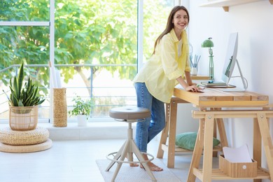 Photo of Woman using computer at wooden desk indoors. Home workplace